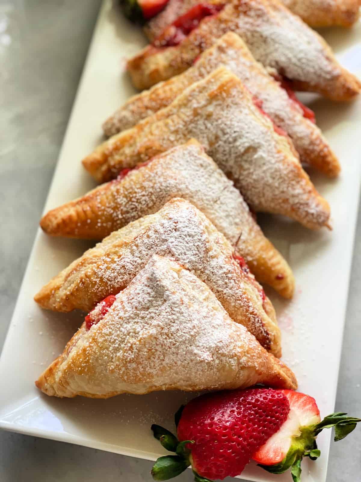 White platter with 6 turnovers dusted with confectioners' sugar.