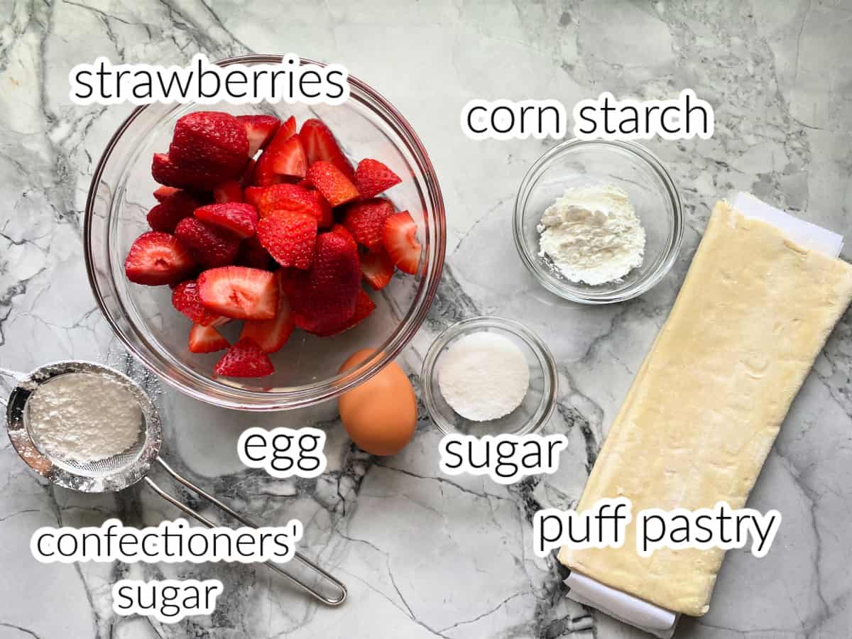 Ingredients on counter: strawberries, cornstarch, sugar, egg, puff pastry, confectioners' sugar