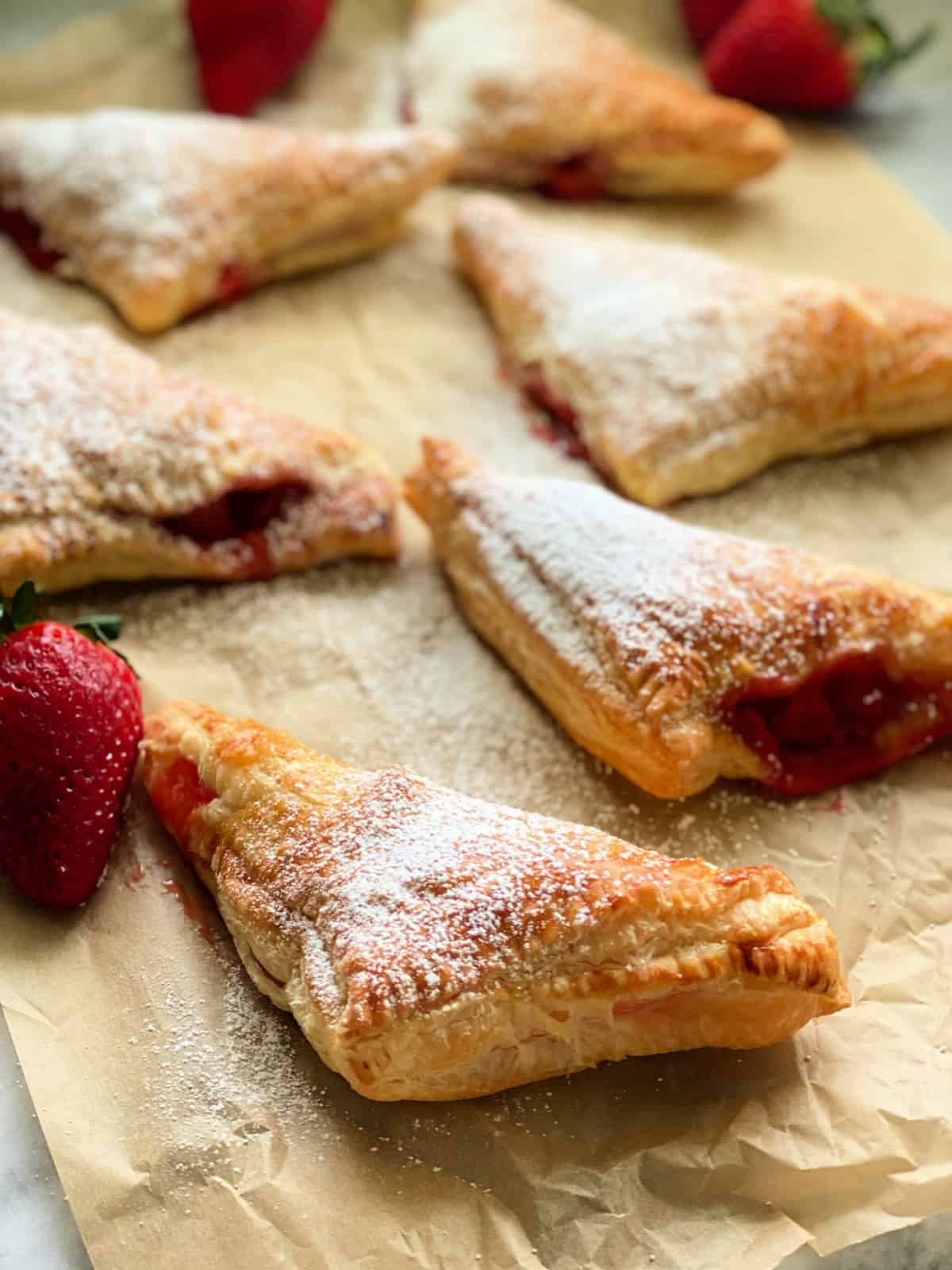 6 triangle turnovers with confectioners' sugar with strawberries on the side.