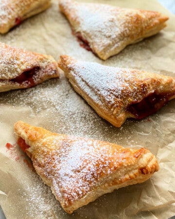 5 triangle turnovers dusted with powdered sugar on brown paper.