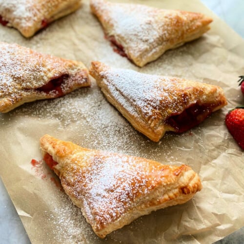 5 triangle turnovers dusted with powdered sugar on brown paper.