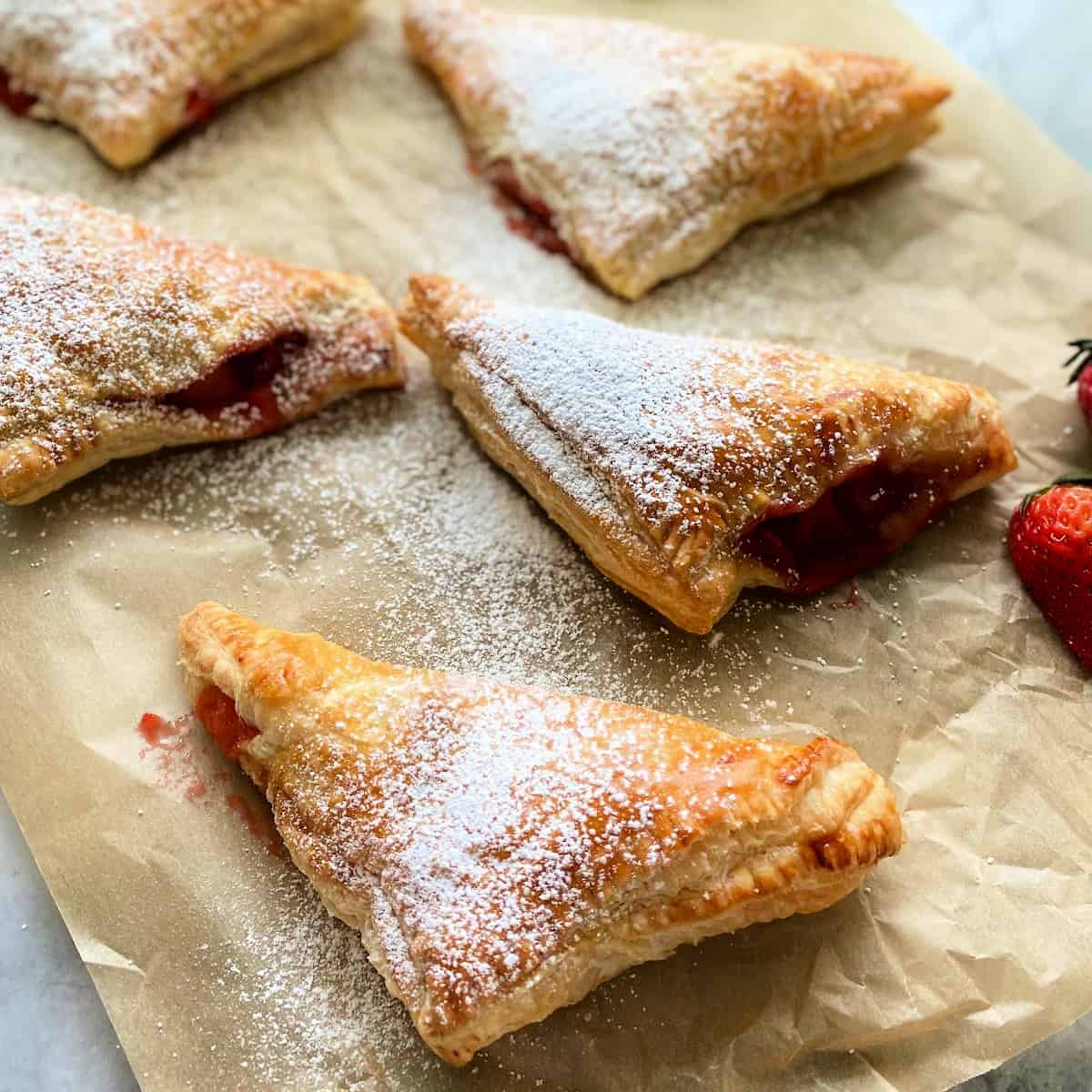 5 triangle turnovers dusted with powdered sugar on brown paper.