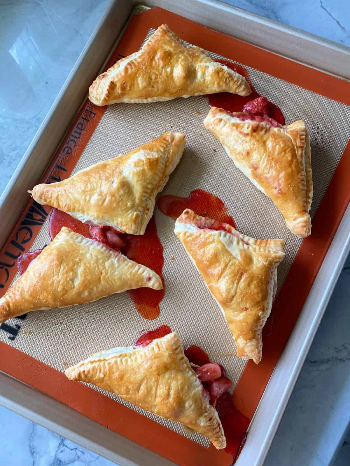Cooked strawberry turnovers on a baking sheet.
