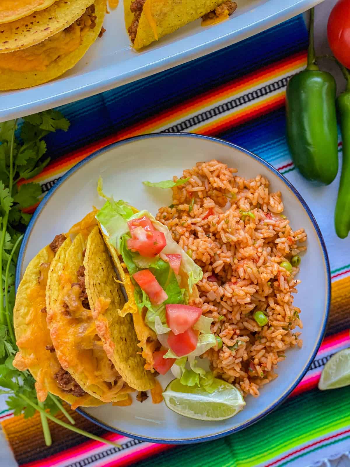 Beef taco served with lettuce, tomatoes, a lime, and rice on a plate.