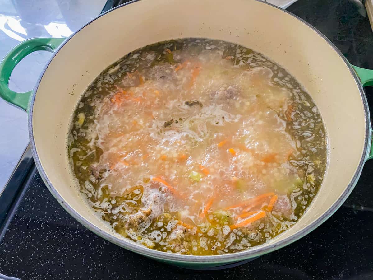 Green pot on stovetop boiling broth.