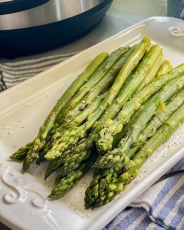 Close up photo cooked asparagus resting on a white ceramic serving dish.