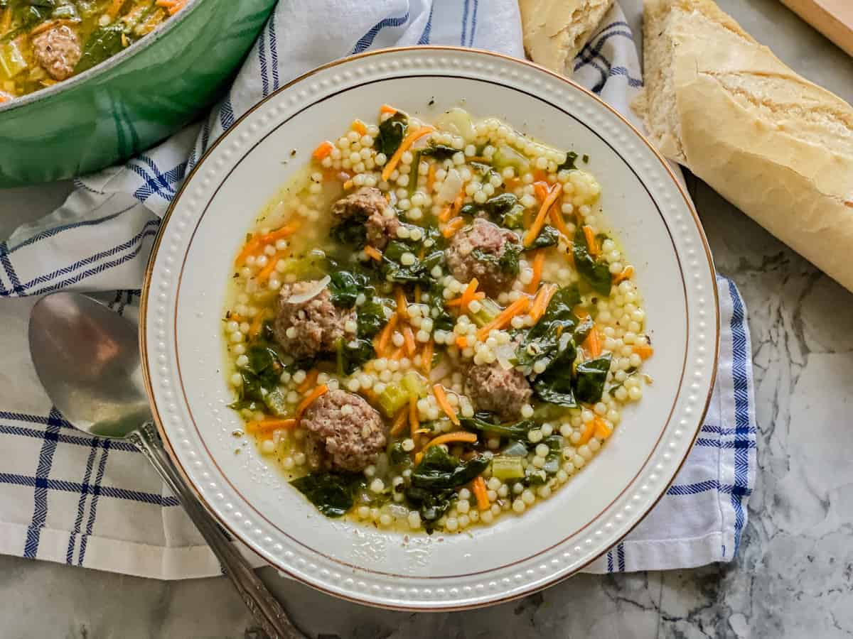 White bowl filled with pastina, shredded carrots, and meatballs on a plaid cloth napkin.