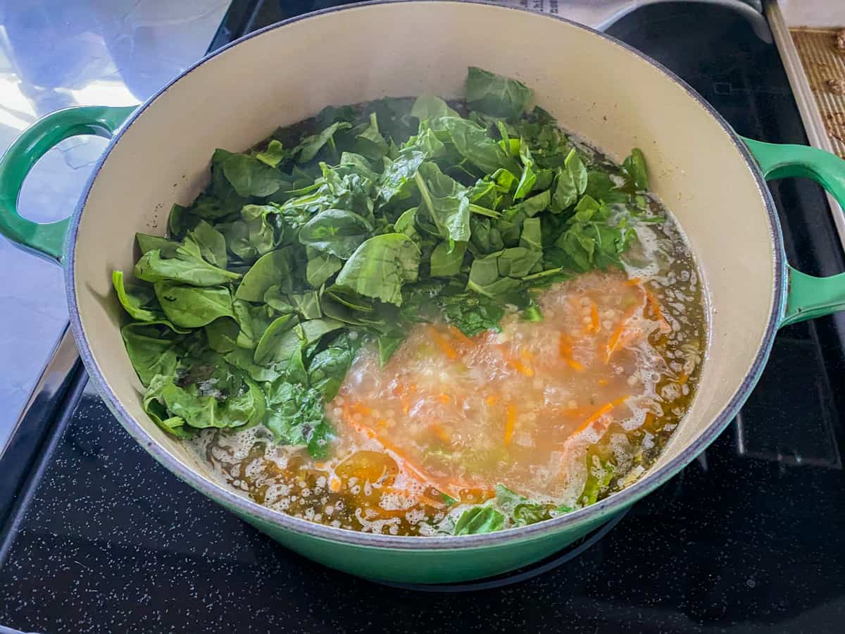 Green pot filled with broth, and chopped spinach.