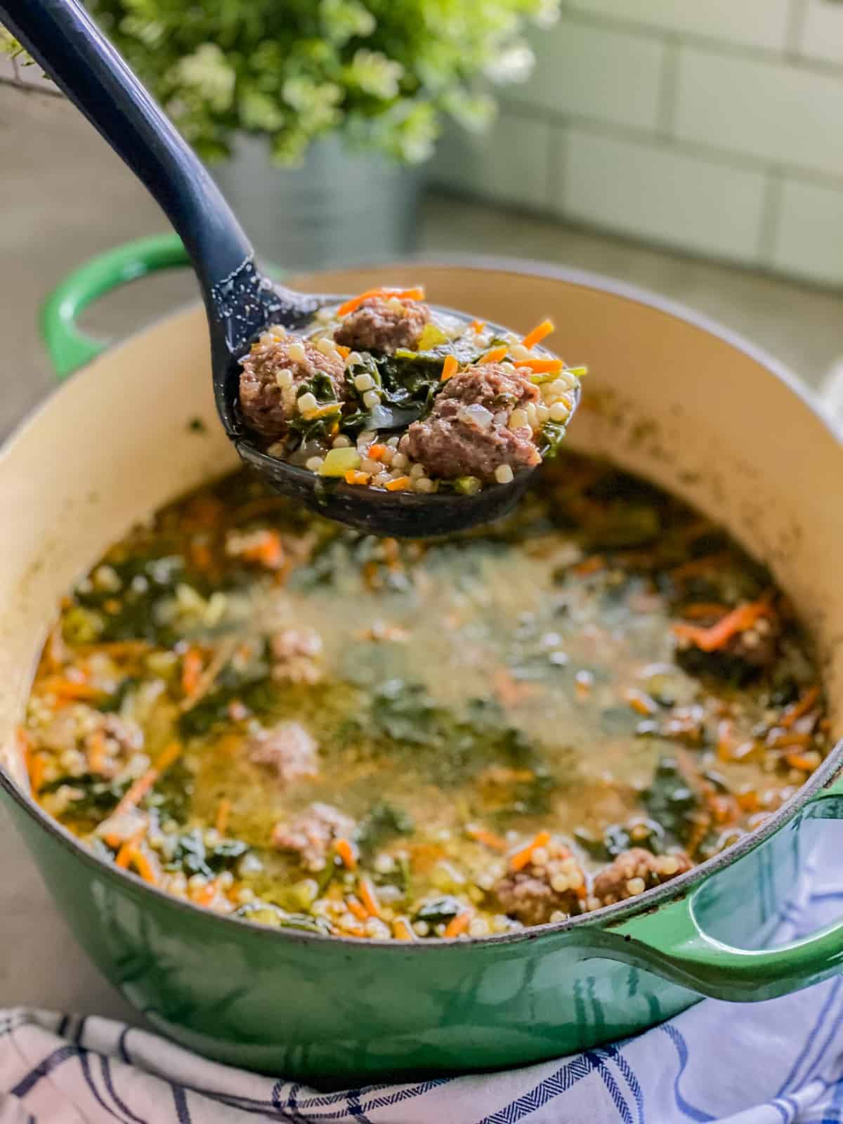 Black ladle holding meatballs, pasta, and veggies over a pot of soup.