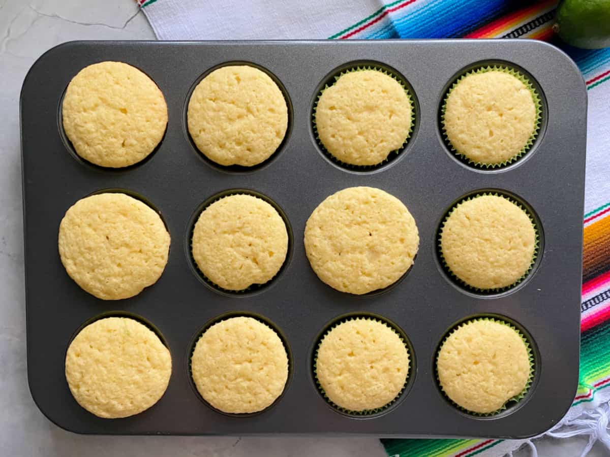 A dozen white cupcakes in a cupcake tray on a marble countertop.