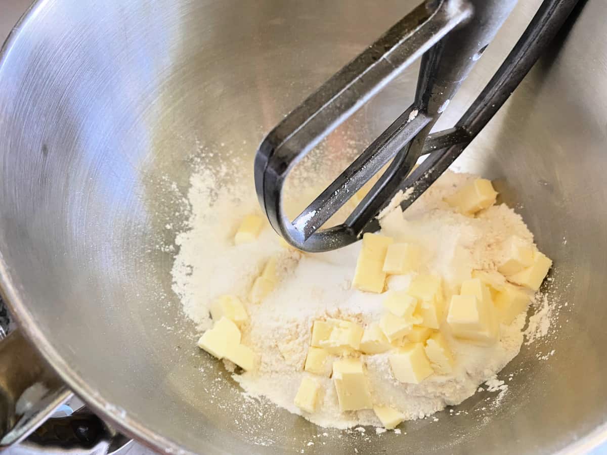 Stainless steel bowl with flour, butter cubes and paddle attachment.