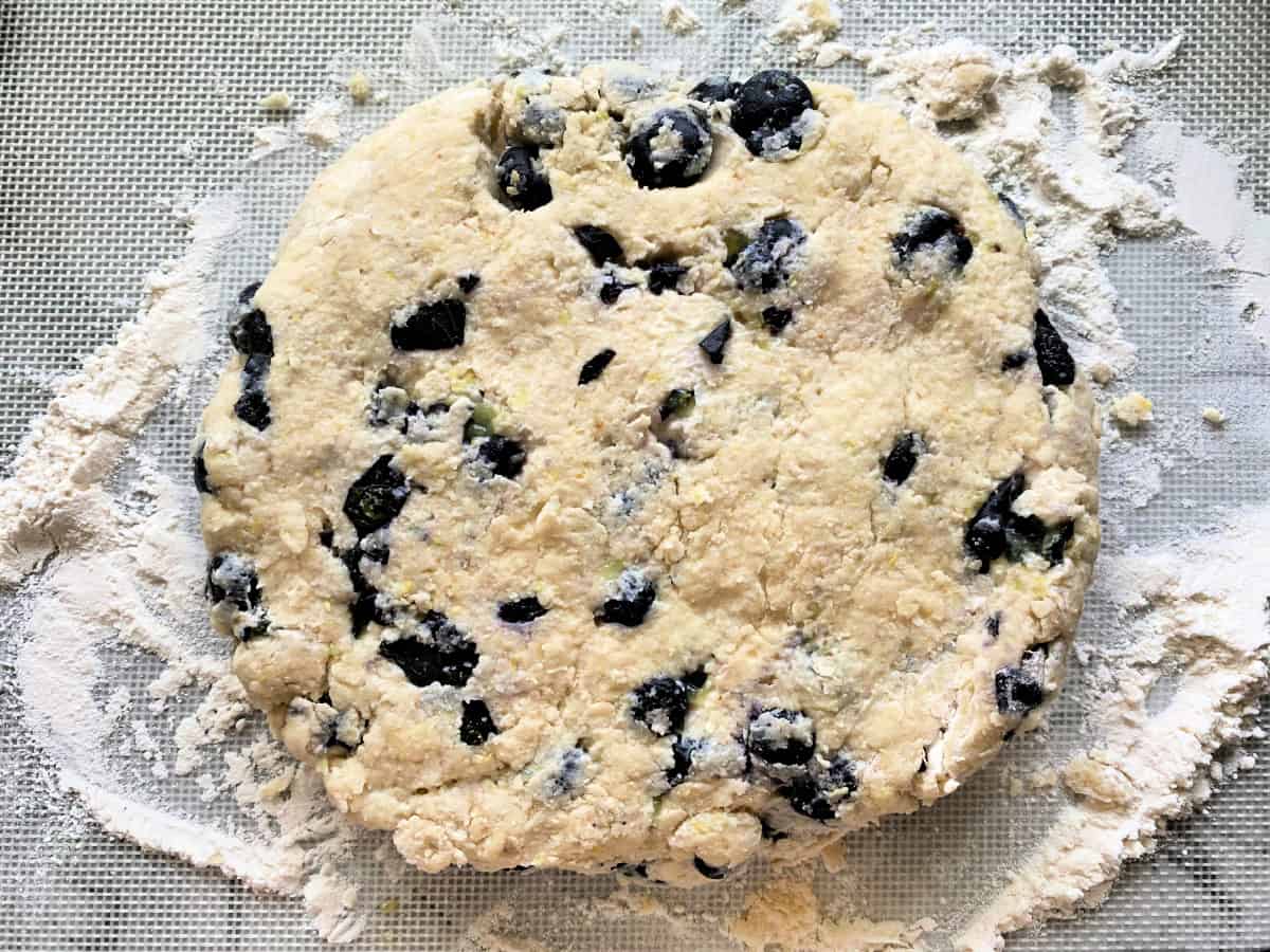 Round disc of blueberry dough on a flour surface.