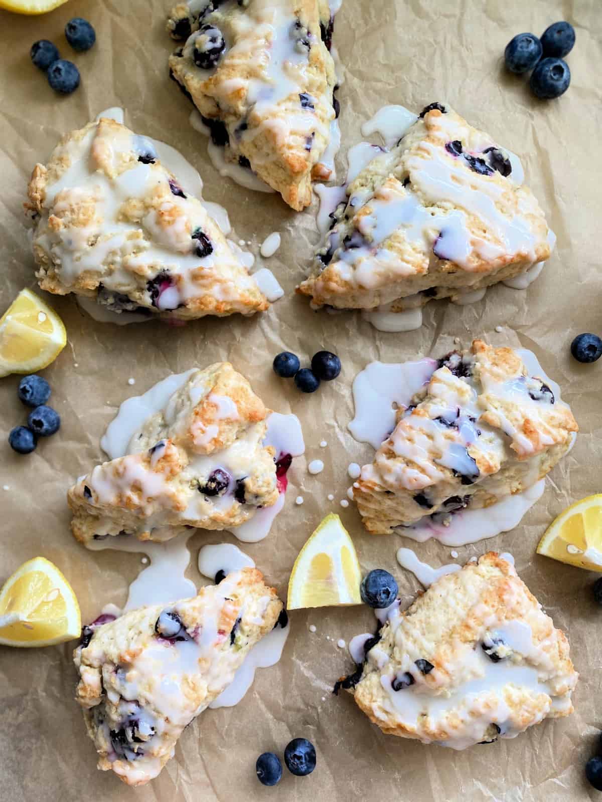 7 scones on brown paper with blueberries and lemon wedges.