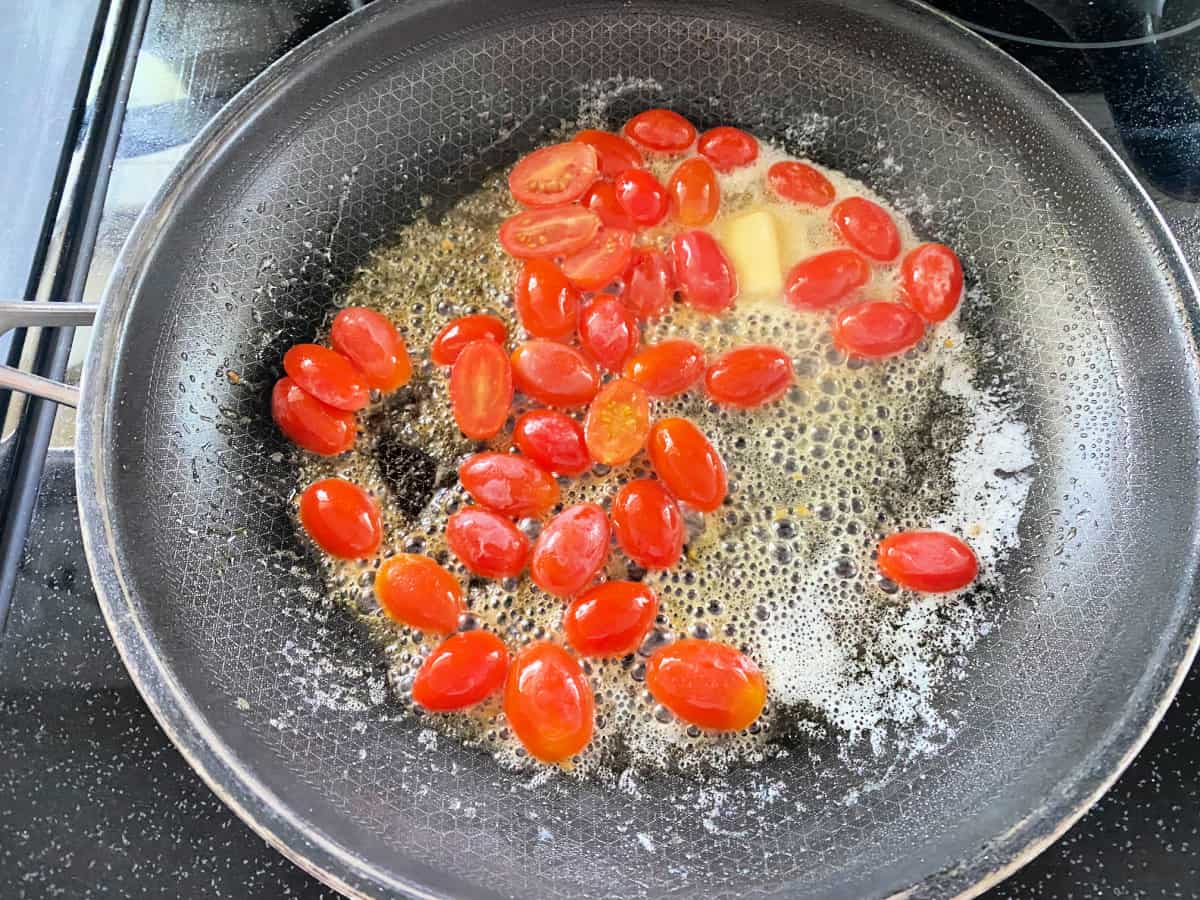 Black frying pan with butter and tomatoes.