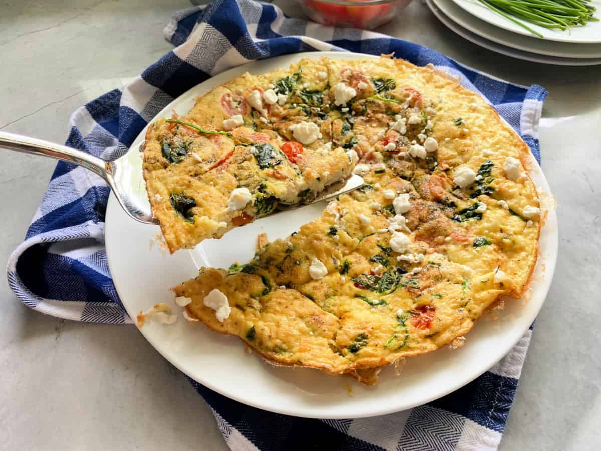 White plate with egg white fritatta with goat cheese with a slice being held over the dish.