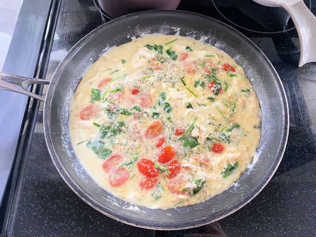 Black pan with set egg whites with tomatoes and spinach.