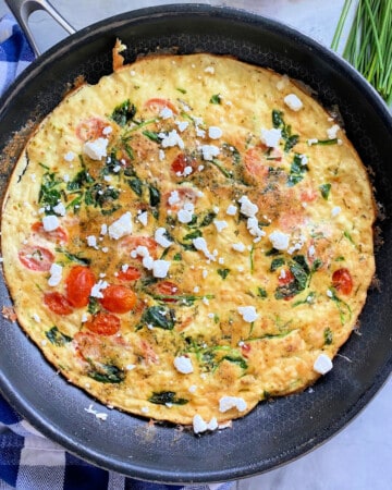Black frying pan with egg white fritatta with goat cheese and herbs.