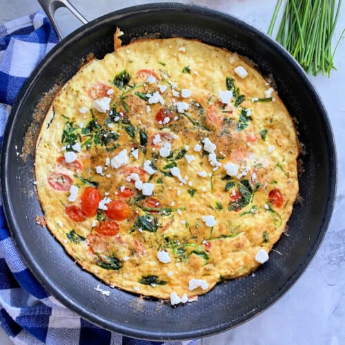 Black frying pan with egg white fritatta with goat cheese and herbs.