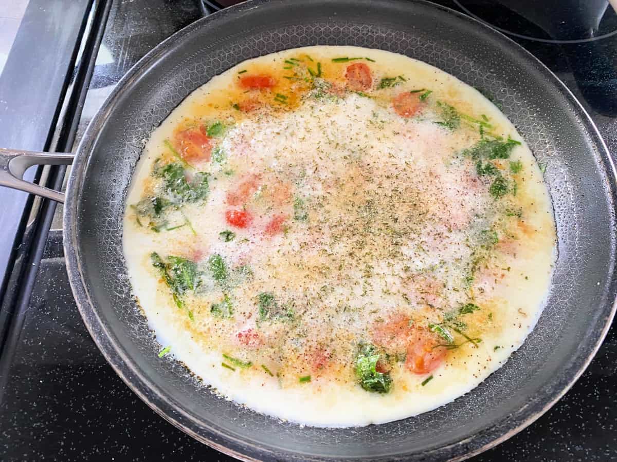 Black saute pan with egg whites, spinach, herbs, and tomatoes.