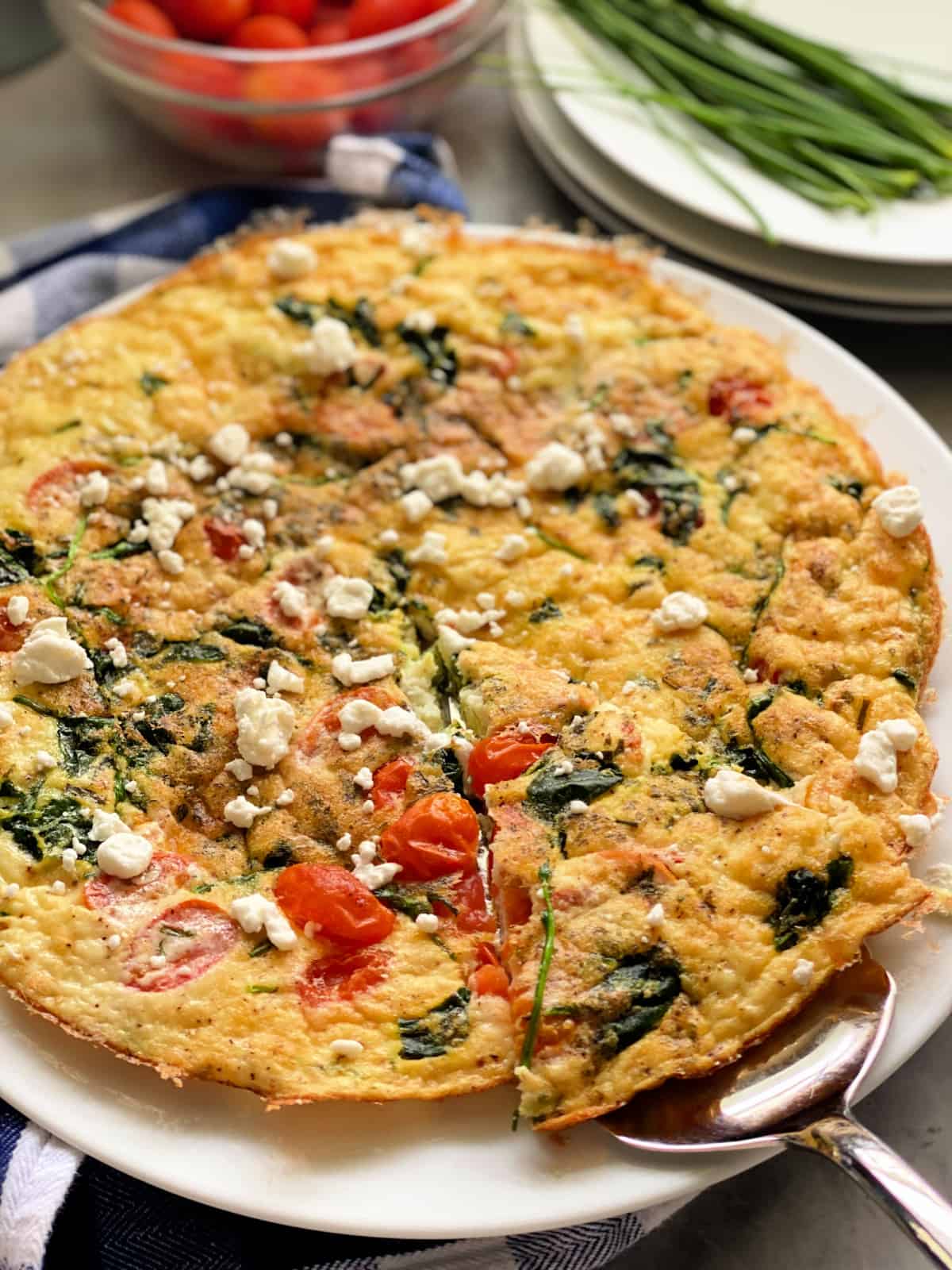Egg fritatta with vegetables and goat cheese with a silver serving utensil pulling a slice out.