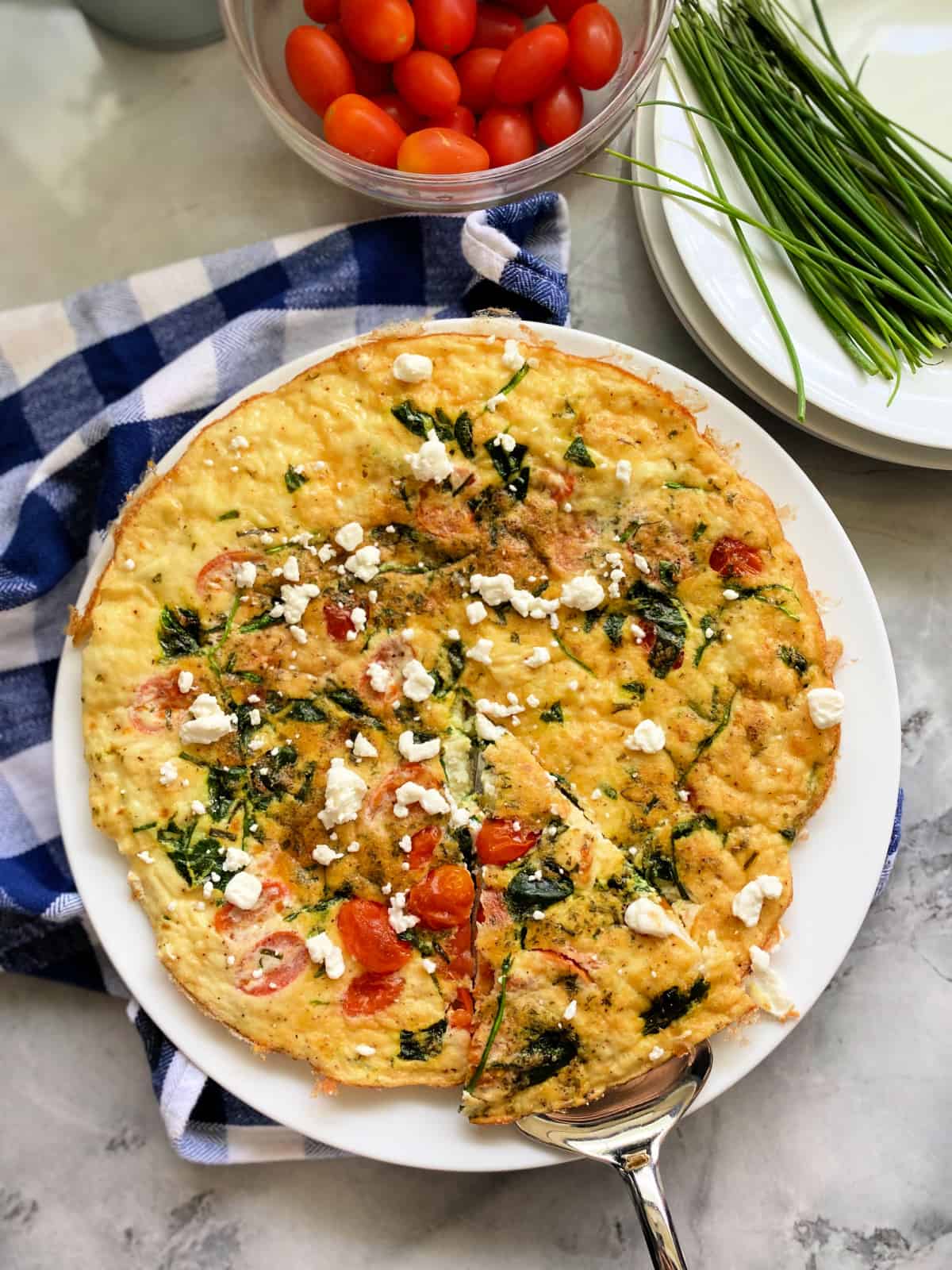 Egg fritatta with a slice being held by a silver serving utensil on a white plate.