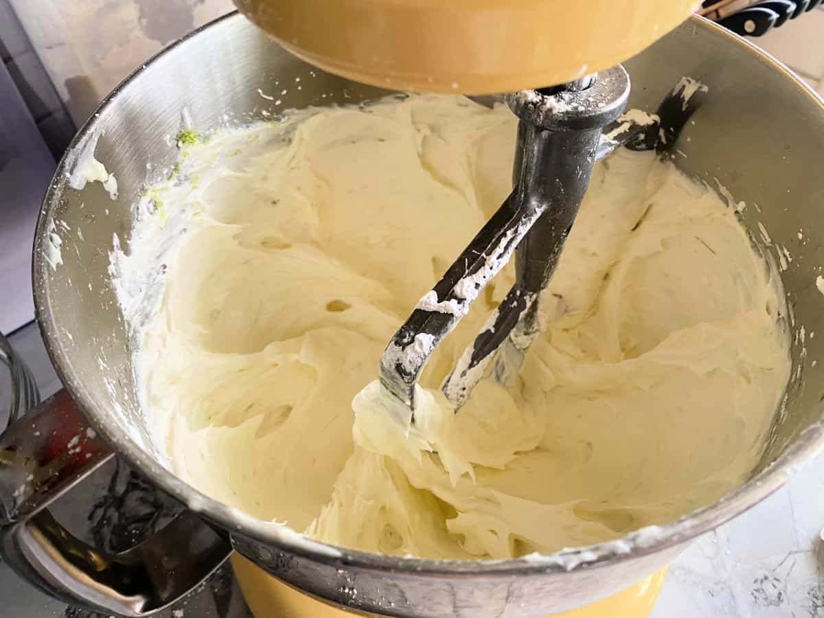 Yellow Kitchenaid mixer fitted with a paddle attachement with white frosting in the bowl.