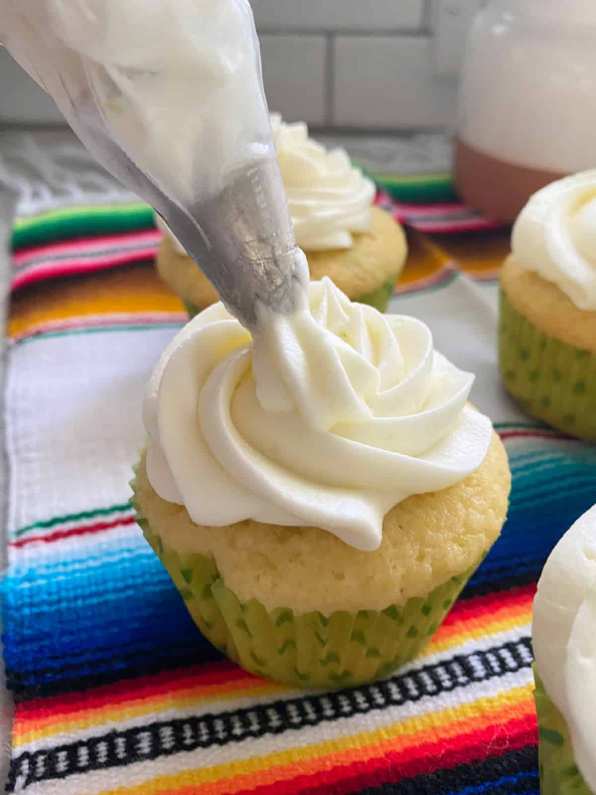 Piping bag piping white frosting onto a white cupcake.