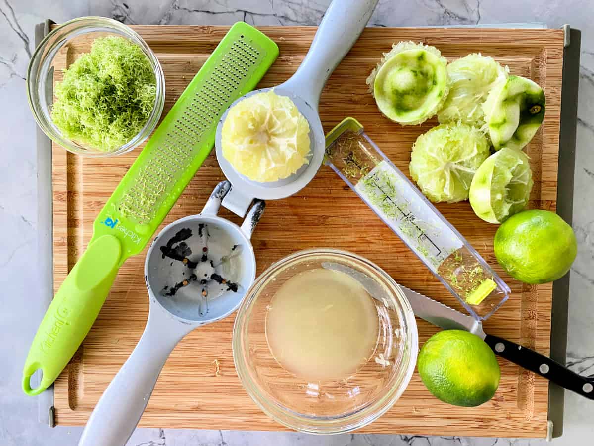 Lime juiced in a hand held lime juicer with other juiced limes next to it and zest in a bowl on the side.