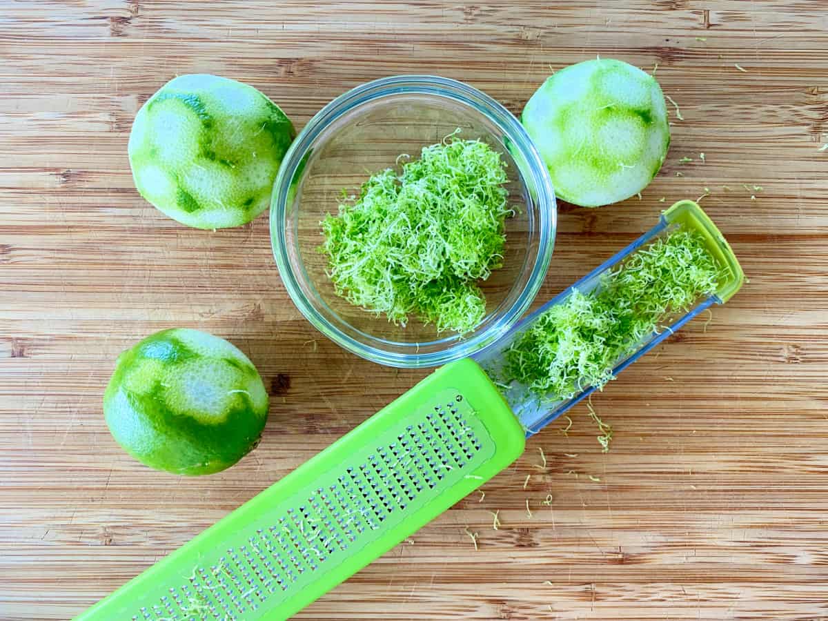 Zester with a bowl of lime zest and zested limes next to it.