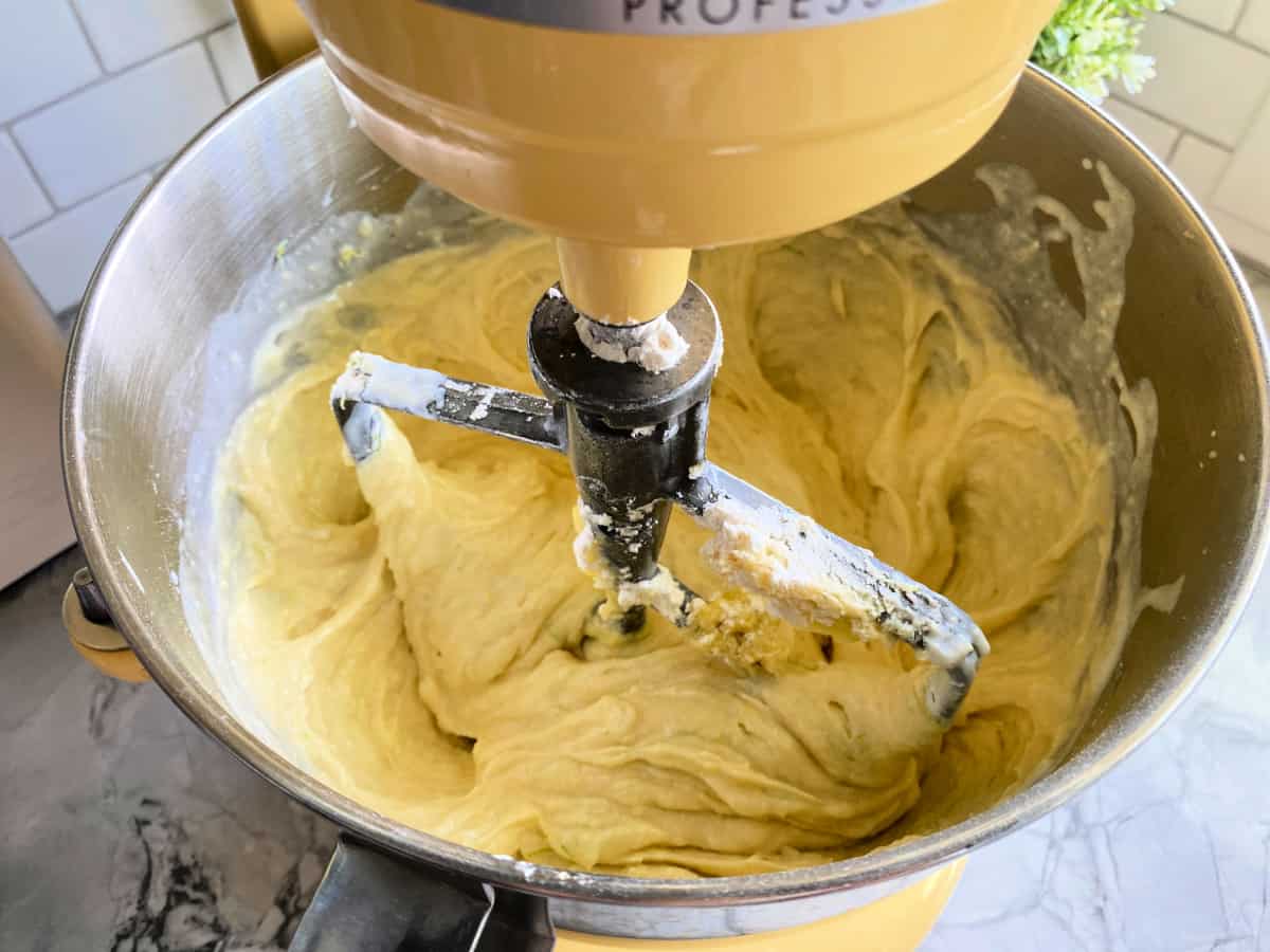 Yellow KitchenAid mixer fitted with a paddle attachment with batter inside the bowl.