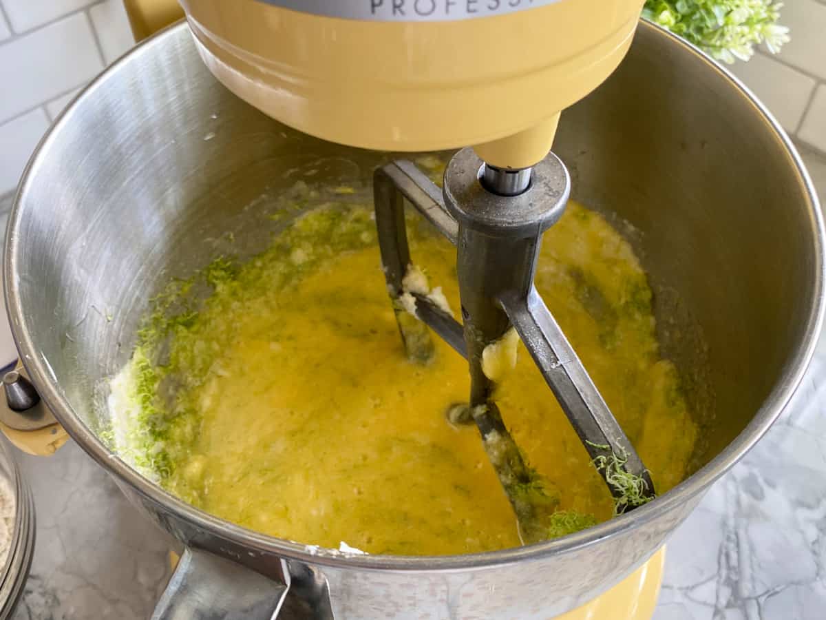 Yellow KitchenAid mixer fitted with a paddle attachment with yellow batter inside the bowl.
