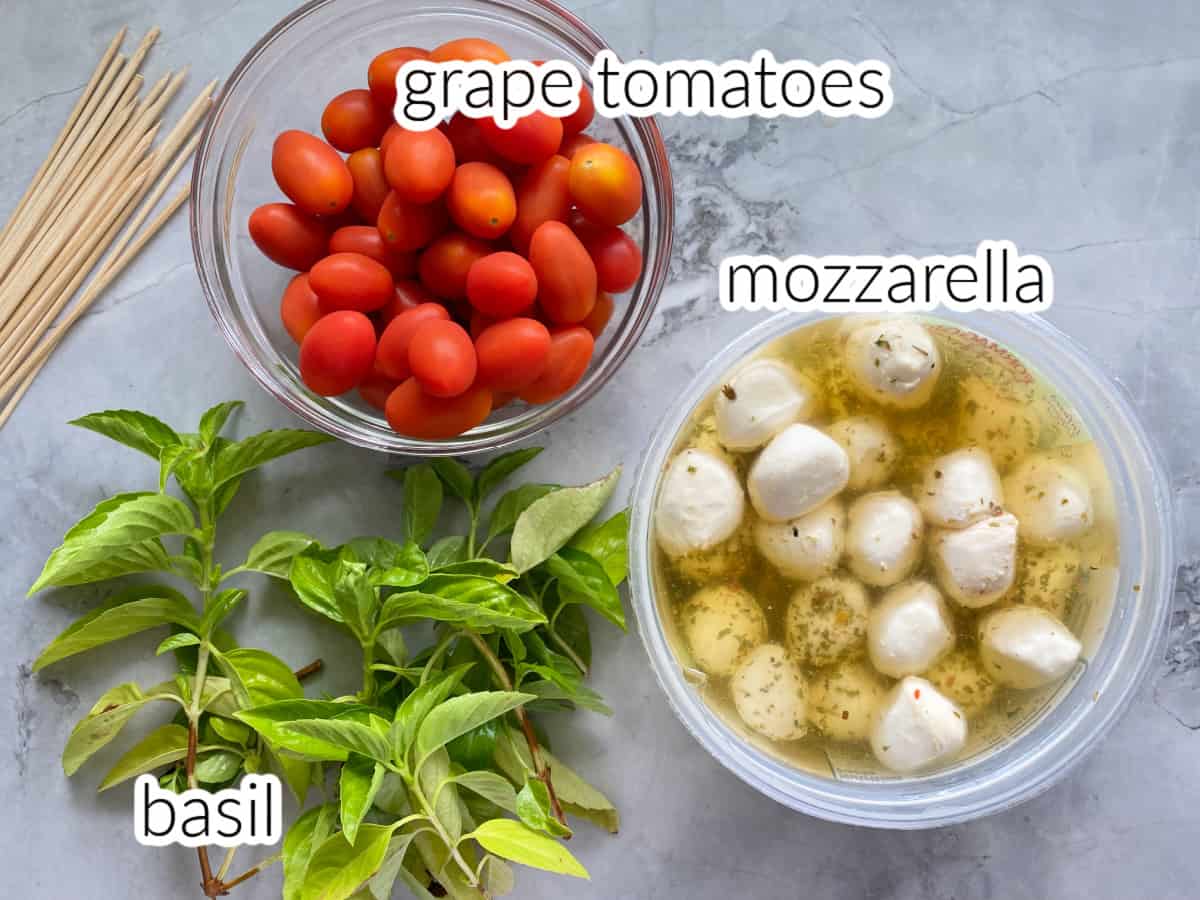 Ingreedients on counter: mini mozzarella, grape tomatoes, basil, and wood skewers.