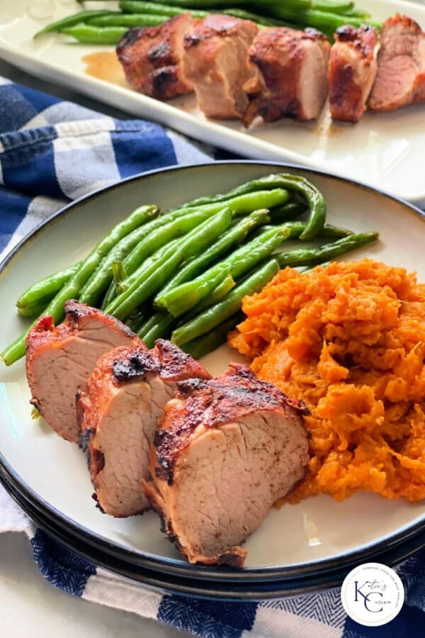 Sliced pork tenderloin with green beans and mashed sweet potatoes with logo on bottom right corner.