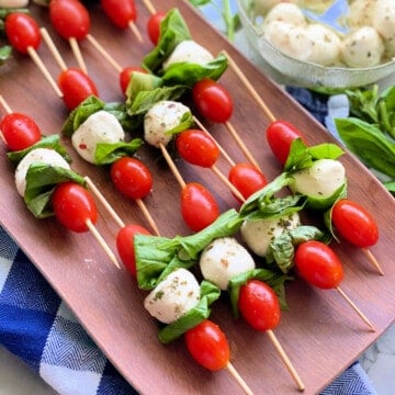 Wood platter filled with skewers filled with grape tomatoes, mozzarella, and basil.