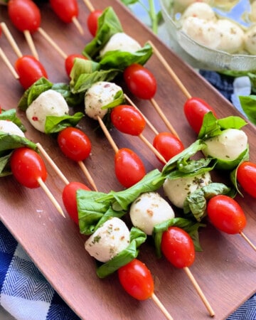 Wood platter filled with skewers filled with grape tomatoes, mozzarella, and basil.