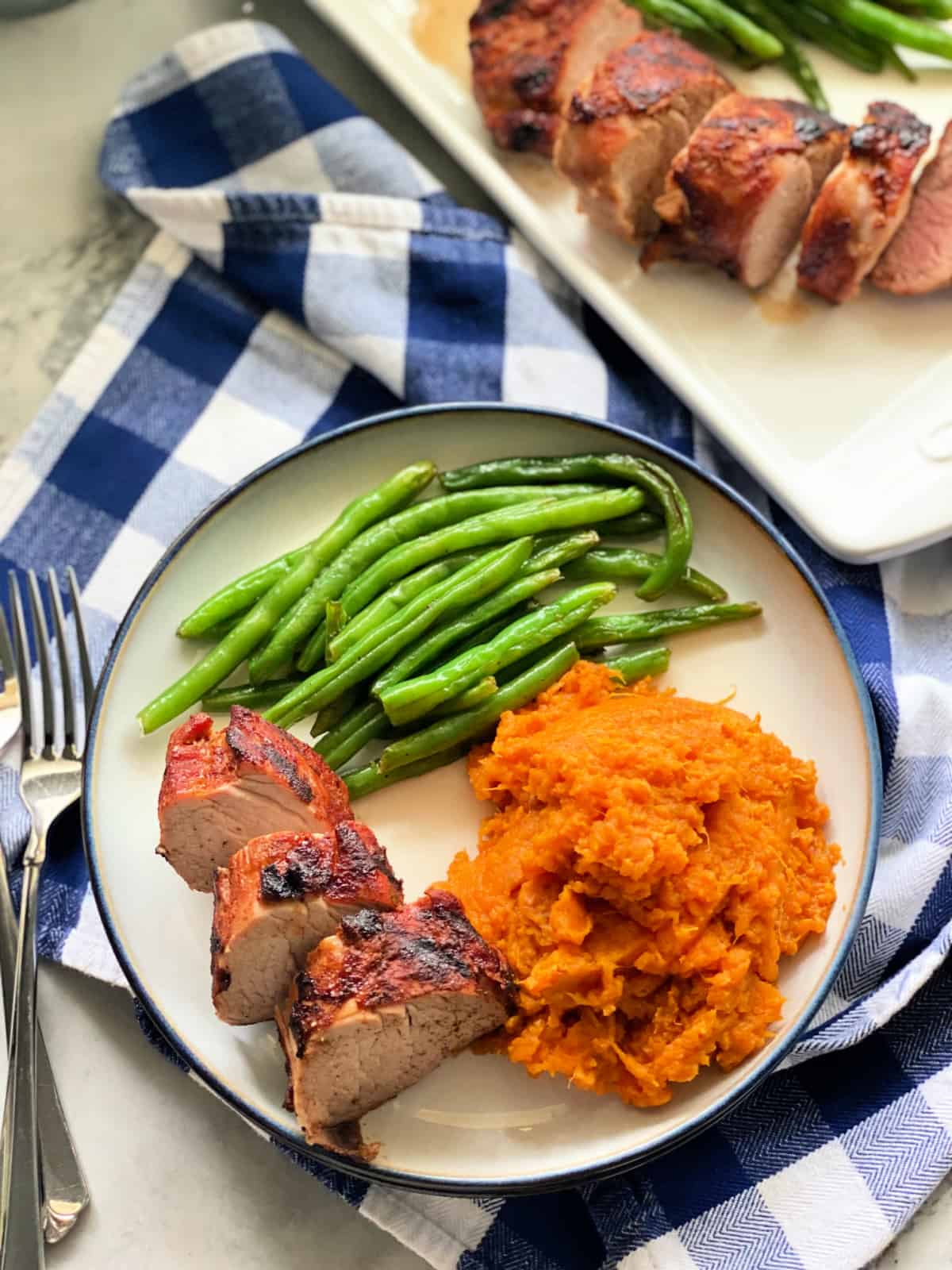 White plate with sliced pork, green beans, and sweet potatoes.