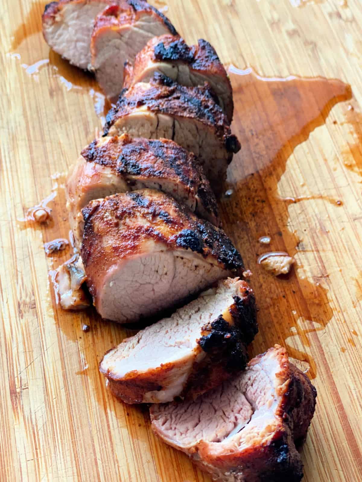 Wood cutting board with sliced grilled pork and juices.