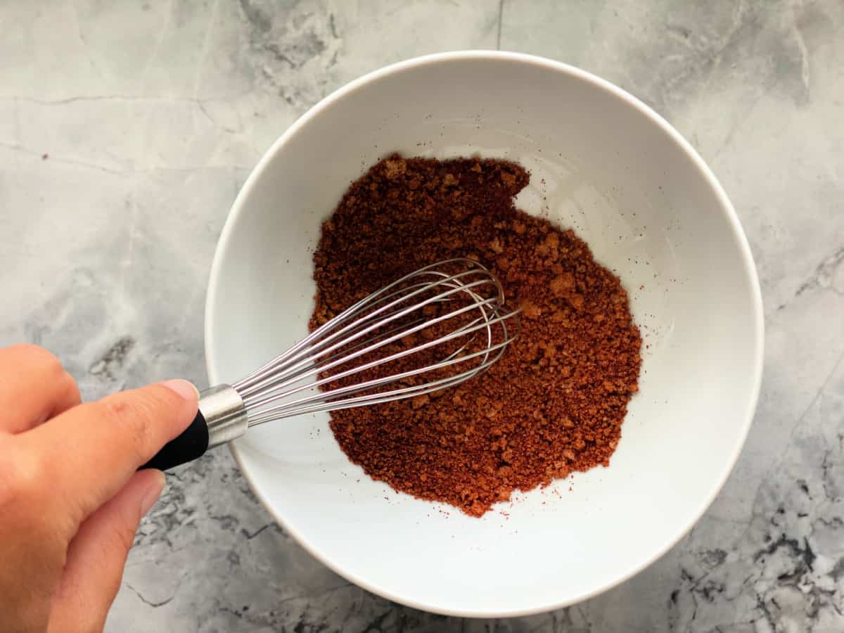 White bowl with hand holding a whisk mixing spices together.