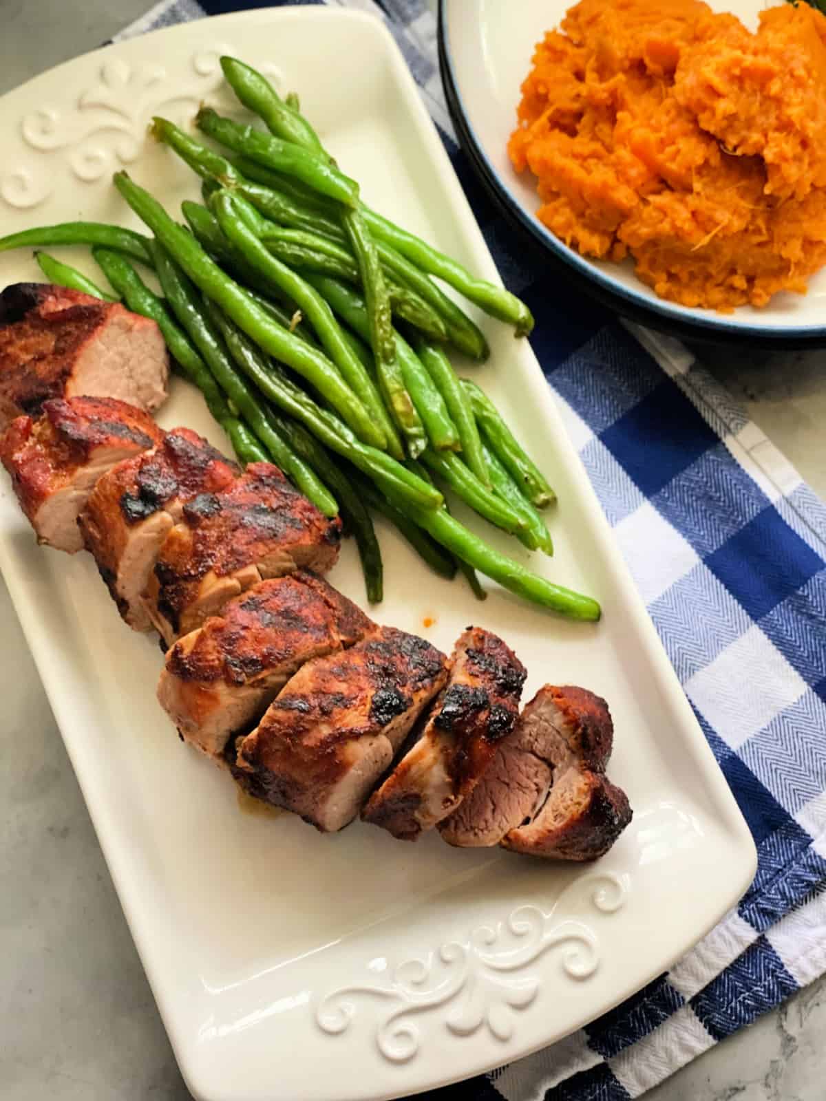 White platter filled with green beans and sliced pork tenderloin.