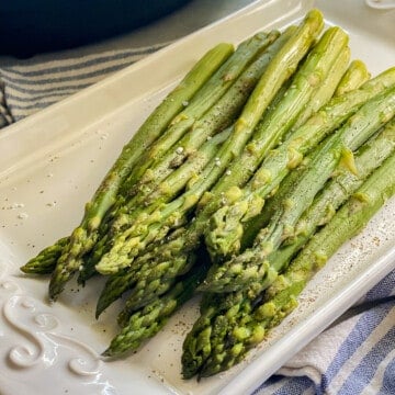 Cooked asparagus on a white platter topped with salt and pepper.
