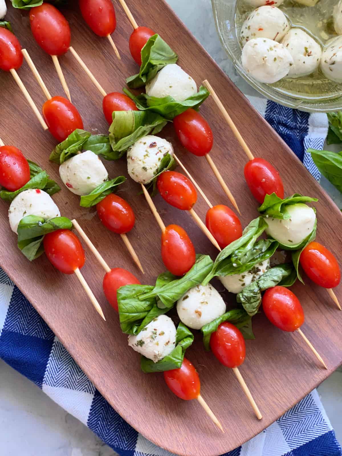 Brown platter filled with skewers with blue and white checkered towel with basil on the bottom.