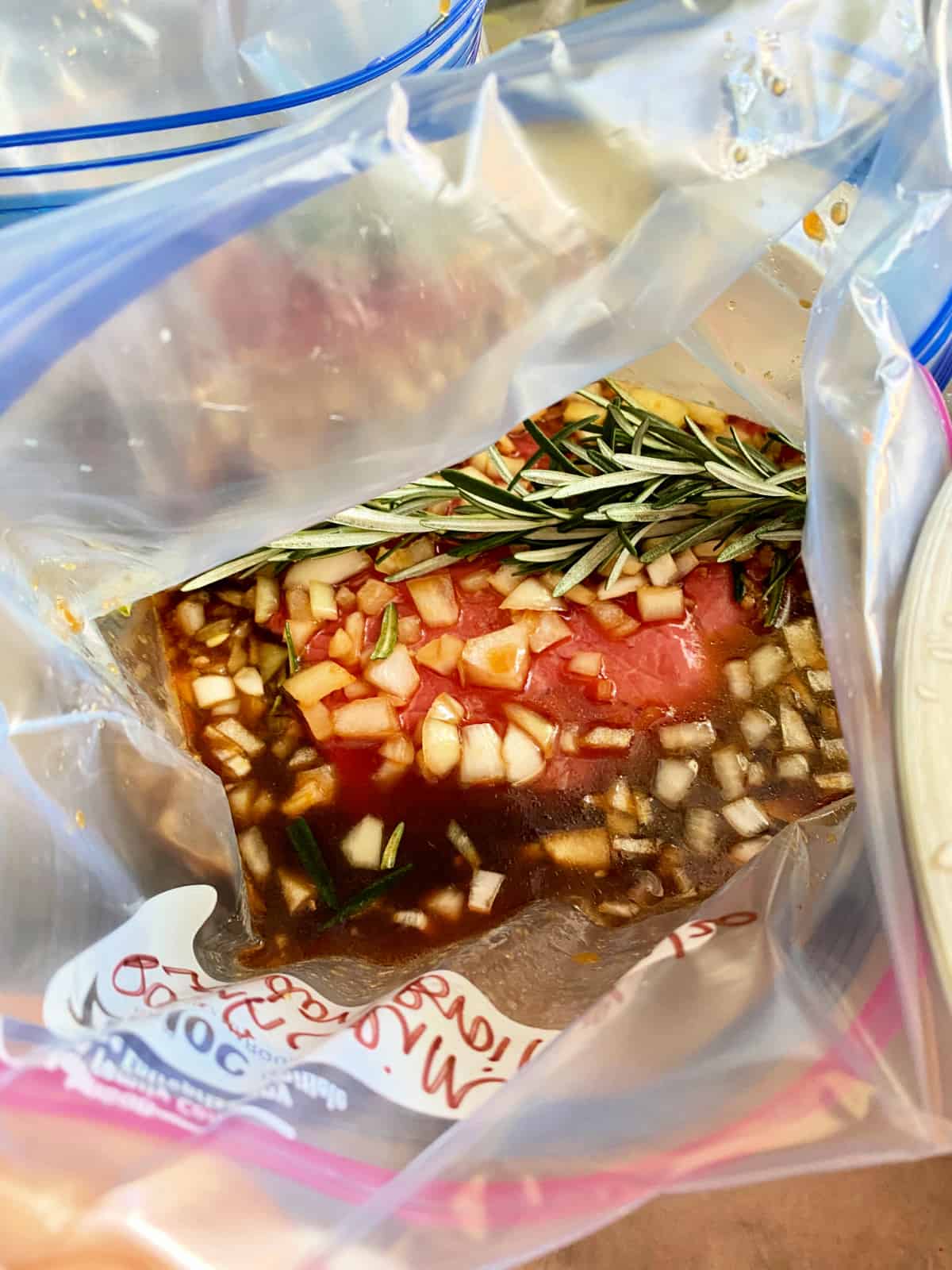 Plastic bag with steak, onions, rosemary and marinade.