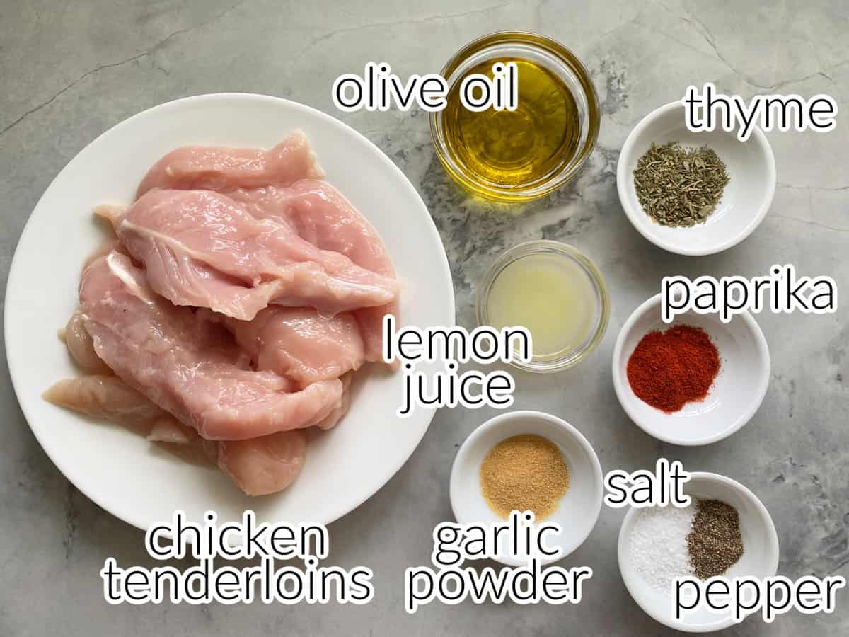 Ingredients on marble counter; chicken tenderloins, olive oil, thyme, paprika, lemon juice, garlic powder, salt, and pepper.