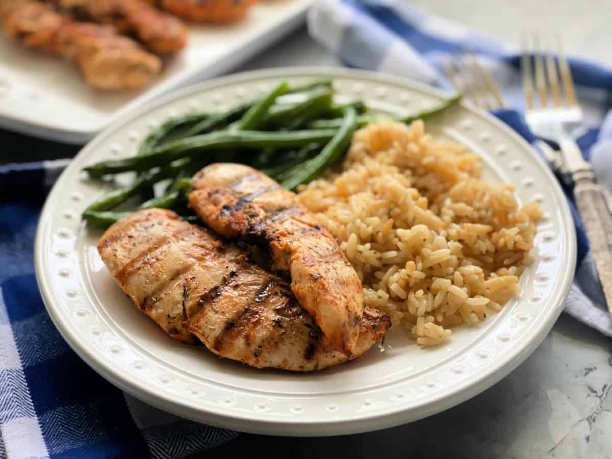 White plate with grilled chicken strips, rice, and green beans.