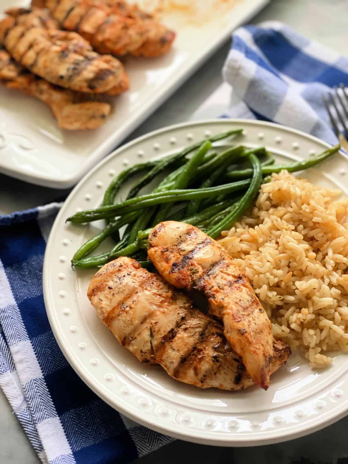 Grilled chicken strips with rice, and green beans with a platter of chicken strips in the background.