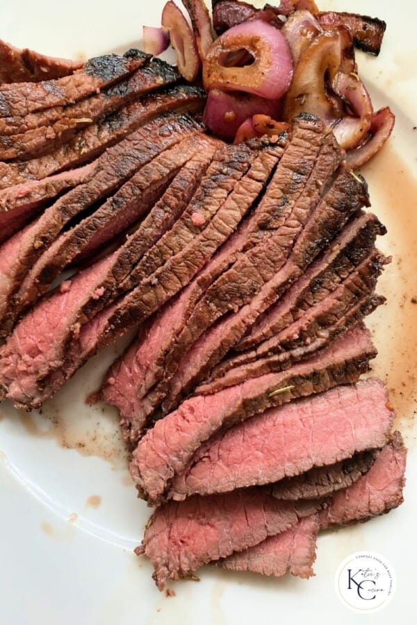 Sliced steak on plate with grilled onions and logo on right corner.
