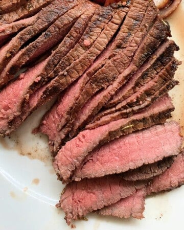 Thinly slices of steak on a white plate with steak juice on plate.