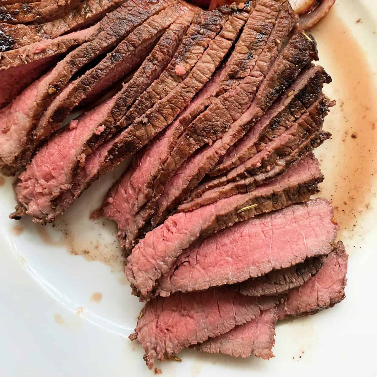 Thinly slices of steak on a white plate with steak juice on plate.