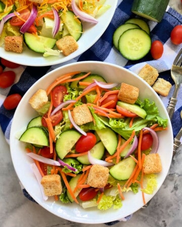 Two white bowls filled with salad and forks and veggies next to it.