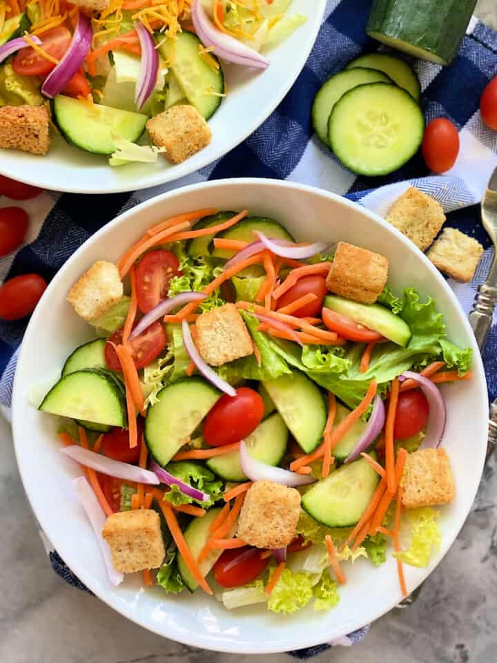 Two white bowls filled with salad and forks and veggies next to it.